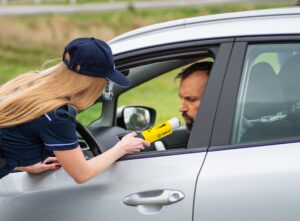 Police officer giving a driver a breathalyzer test through a car window, a check that can follow a drunk driving accident