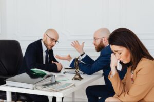 Emotional client sitting with two attorneys discussing paperwork at a law office desk, illustrating how to settle an auto accident claim with a lawyer
