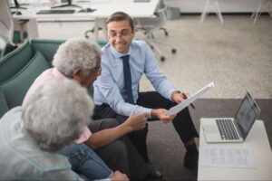 Advisor pointing to paperwork while explaining details to two clients seated nearby, illustrating who is the adjuster in an auto accident