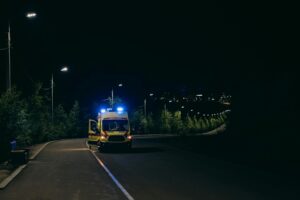 Ambulance with lights on parked on a dark road at night, responding to a scene that could involve a hit and run accident