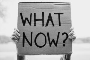 Person holding a cardboard "What Now?" sign, representing what to ask a truck accident lawyer after a crash